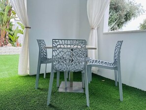 A corner seating area with a metal table and chairs, surrounded by white walls and a window with white curtains. - Oasi Cleopatra Luxury suite B&B (Manduria)