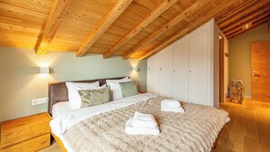 Une chambre avec un plafond en bois, un lit recouvert de draps blancs et une armoire.