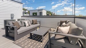 Eine Dachterrasse mit einer grauen Sofagruppe, einem Couchtisch und Lichterketten.