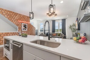 A modern kitchen with a large island, a built-in oven, and a hanging light fixture. - 2 Luxury Homes Side-by-Side | 2 Rooftop Hot Tubs (nashville)
