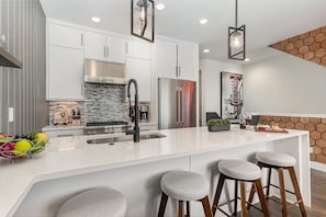 A modern kitchen with white cabinetry, stainless steel appliances, and a central island with bar stools. - 3 Side-by-Side Homes | 12BR | 3 Rooftop Hot Tubs (nashville)