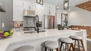 Een moderne keuken met witte kasten, roestvrijstalen apparatuur en een centraal kookeiland met barstoelen.