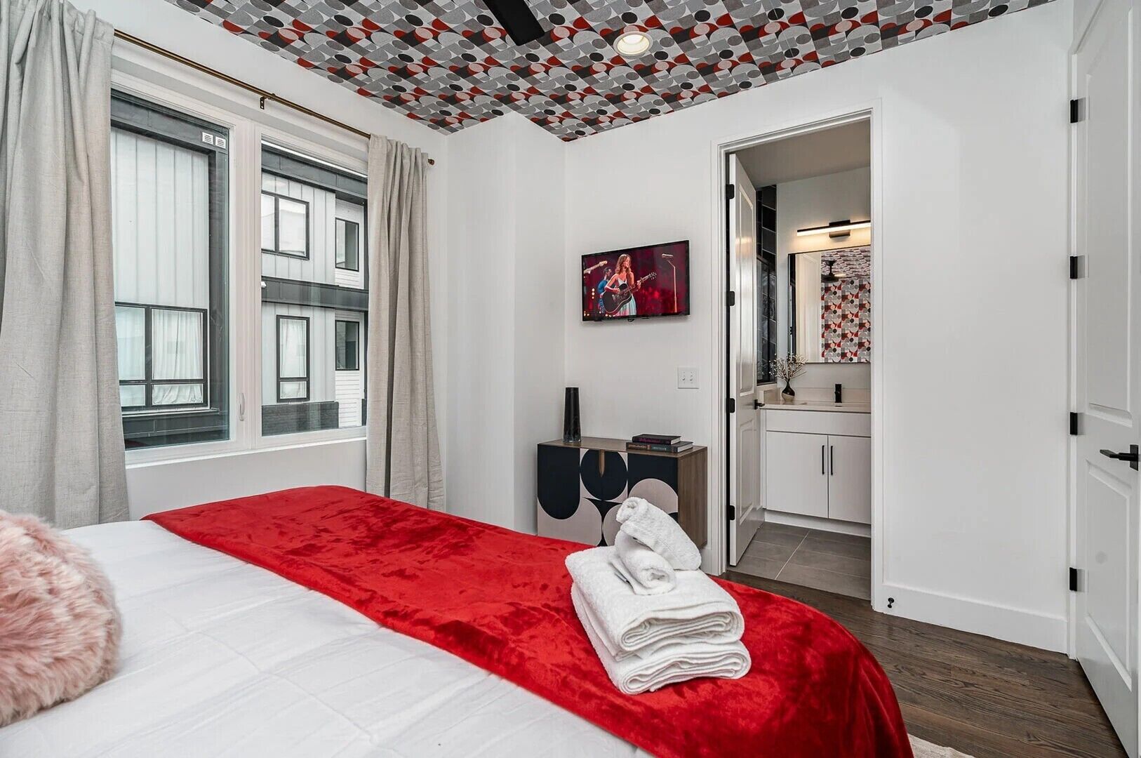 A hotel room with a bed, a TV, a desk, and a bathroom visible through an open door.