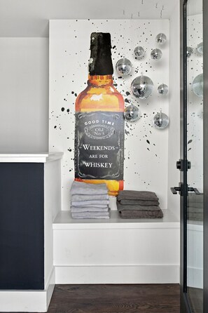 A wall with a large whiskey bottle illustration, disco balls, and folded towels. - Luxury Skyline Rooftop Hot Tub | 5 Min to Broadway (nashville)