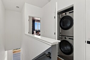 Ein Waschraum mit zwei übereinander gestapelten Waschmaschinen, einem kleinen Fenster und einer weißen Ablage.