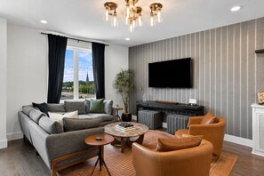 Ein modernes Wohnzimmer mit einer Couch, Sesseln, einem Couchtisch und einem flachbildfernseher an der Wand.