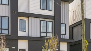Un immeuble résidentiel moderne à plusieurs étages, doté d’un toit plat, de grandes fenêtres et d’un jardin bien entretenu à l’avant.