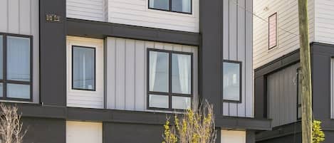 A modern multi-story residential building with a flat roof, large windows, and a well-maintained front yard.