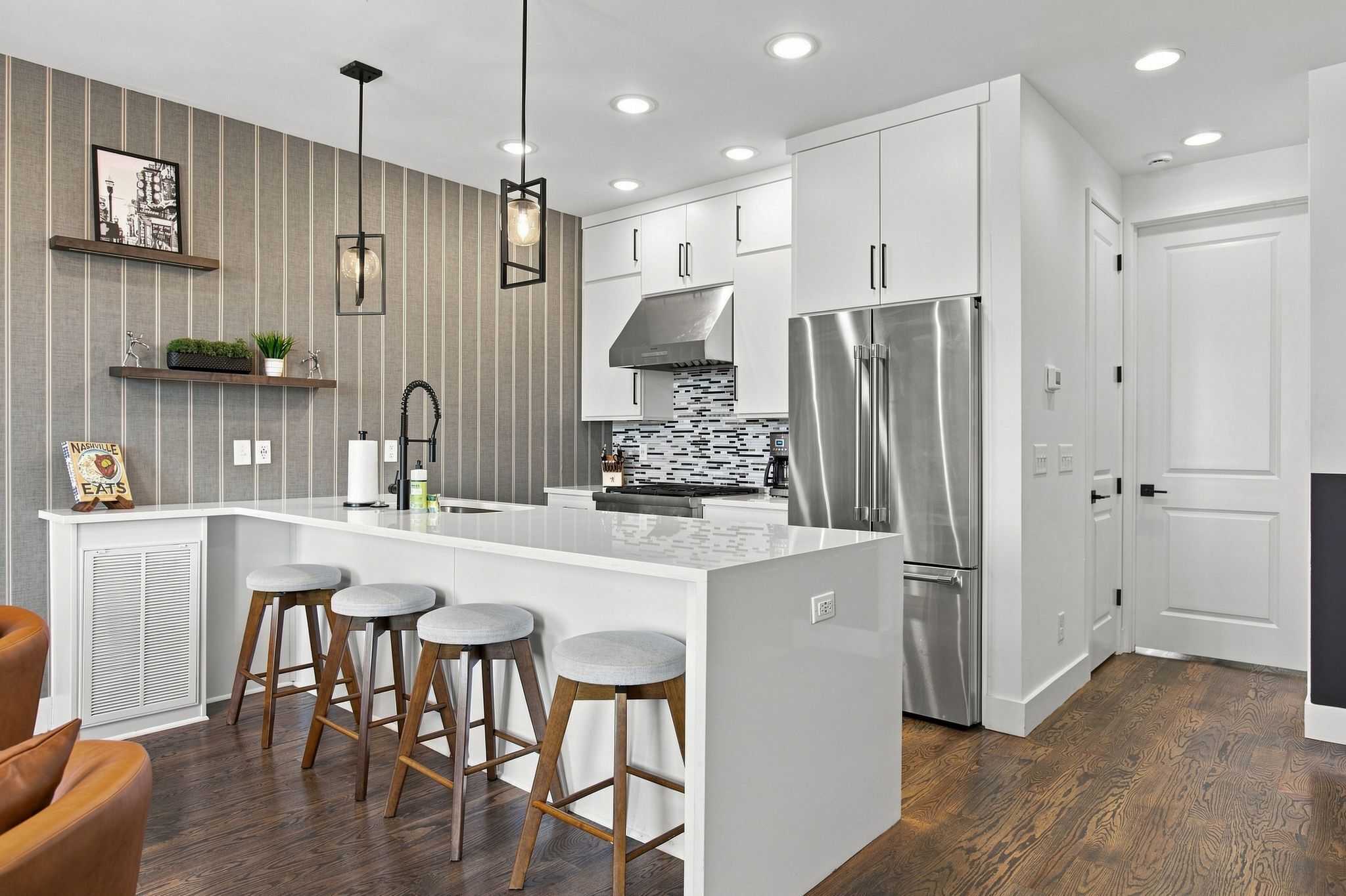 A modern kitchen with a central island, bar stools, stainless steel appliances, and a decorative backsplash.
