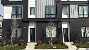 Een modern herenhuis met twee verdiepingen, een zwart-wit gevel, grote ramen en een verzorgde voortuin.