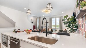 Een moderne keuken met een groot schiereiland, roestvrijstalen apparatuur en hangende lampen.
