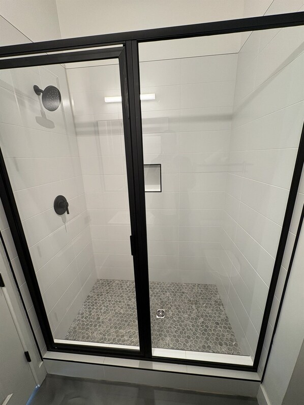 Een douche met glazen wand, witte tegels en een zwart frame.