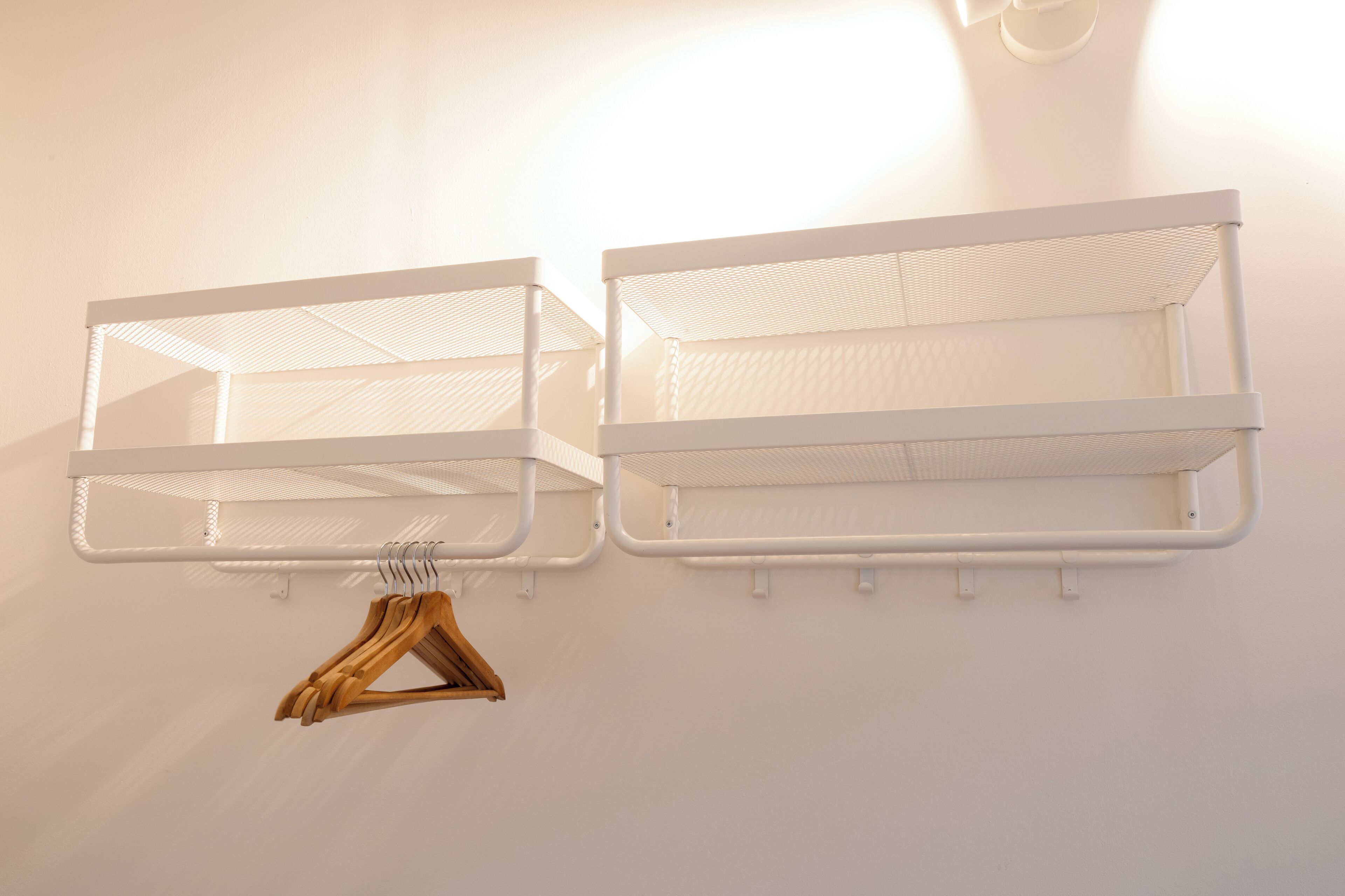 Deux étagères métalliques blanches, fixées au mur, avec un porte-manteau en bois en dessous.
