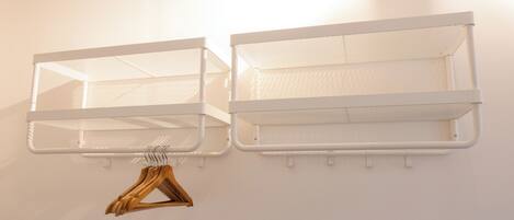 Deux étagères métalliques blanches, fixées au mur, avec un porte-manteau en bois en dessous.