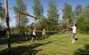 A group of people playing volleyball on a grassy field with trees in the background. - Yart (Scharendijke)