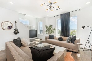 A modern living room with a sofa, coffee table, and a guitar on the wall. - Spacious 4BR Luxury Stay w/ Rooftop Hot Tub (nashville)