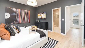 Un dormitorio moderno con cama, una consola negra, un televisor y un cuadro abstracto grande en la pared.