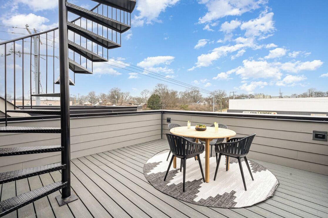 A rooftop terrace with a round table and chairs, a spiral staircase, and a view of the cityscape.