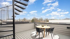 Una terraza en la azotea con una mesa redonda y sillas, una escalera de caracol y vistas de la ciudad.