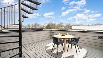 A rooftop terrace with a round table and chairs, a spiral staircase, and a view of the cityscape.