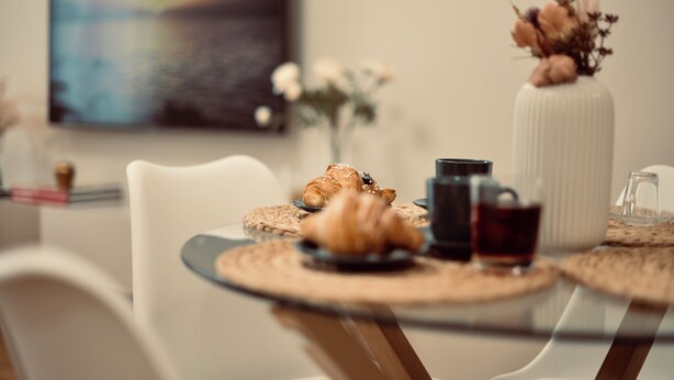 Une table à manger avec des croissants, une cafetière et un verre contenant un liquide sombre, probablement du café ou du thé.