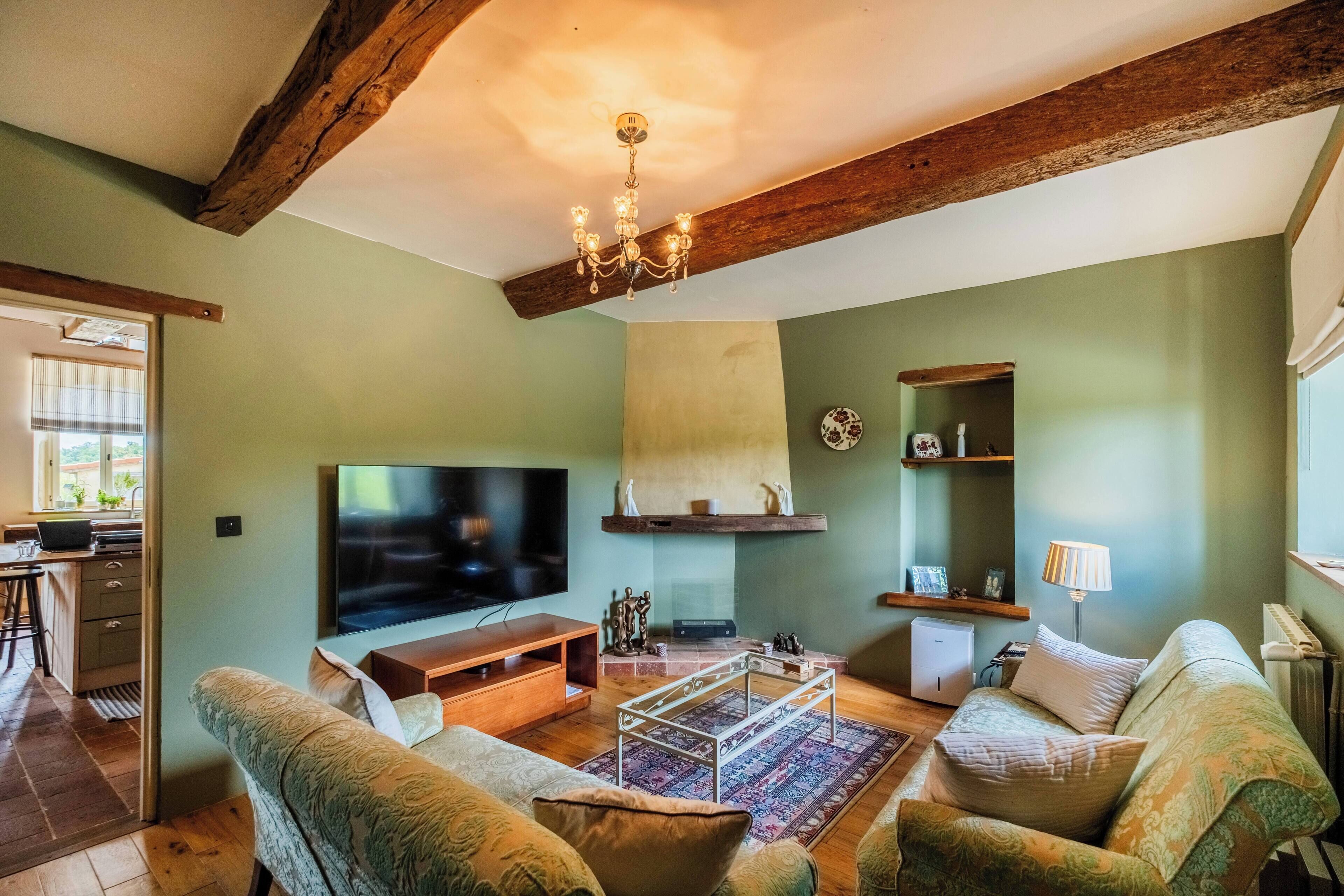 A cozy living room with a television, sofa, coffee table, and wooden beams on the ceiling.