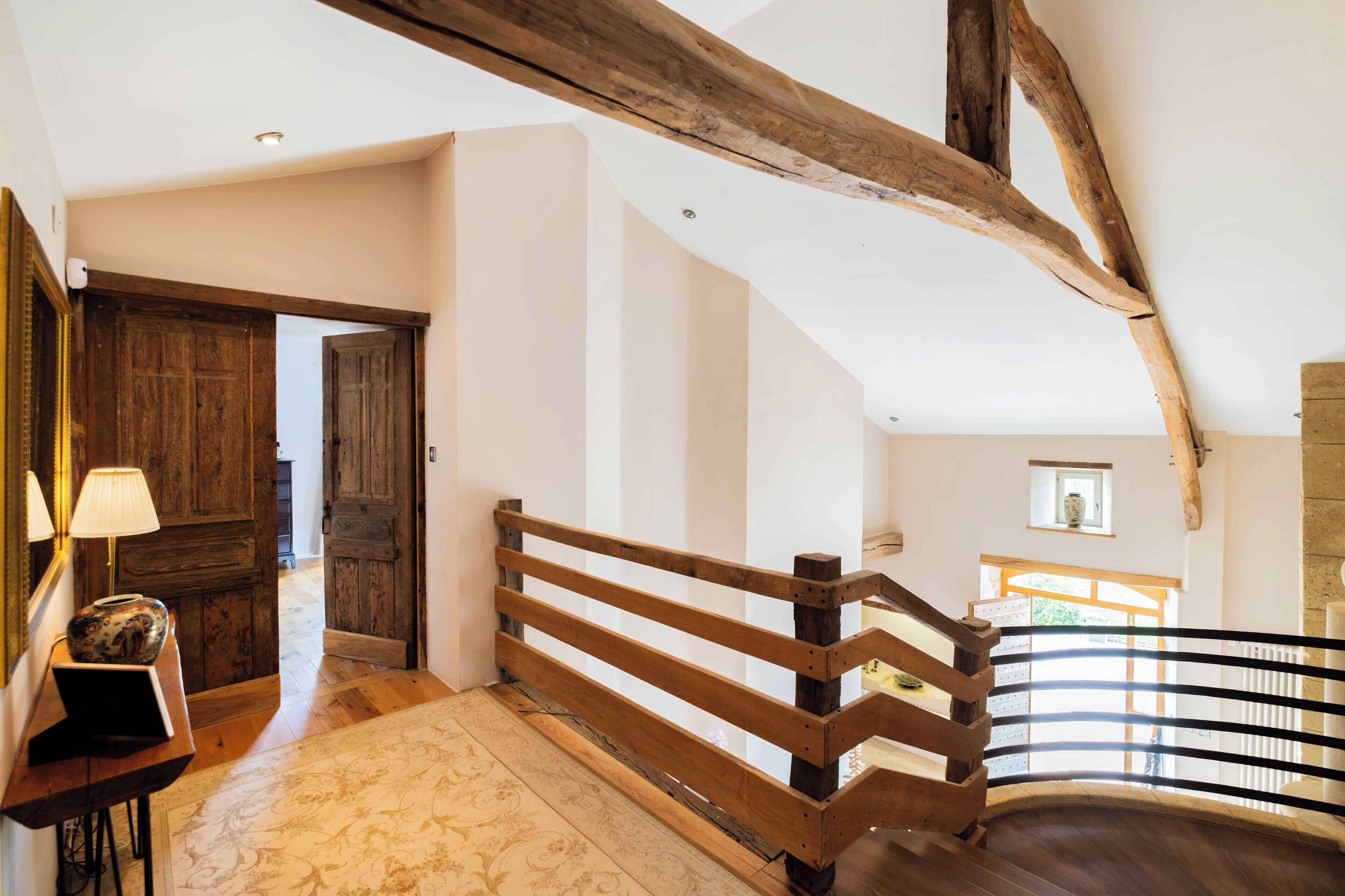 Un escalier en bois avec une rampe, une porte en bois et une petite fenêtre ornée d’un vase.