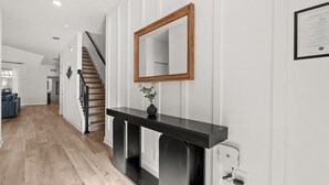 A modern interior with a wooden staircase, a black console table with a vase, and a framed certificate on the wall. - Family 5BR Villa w Pool Theatre Reunion Village (Kissimmee)