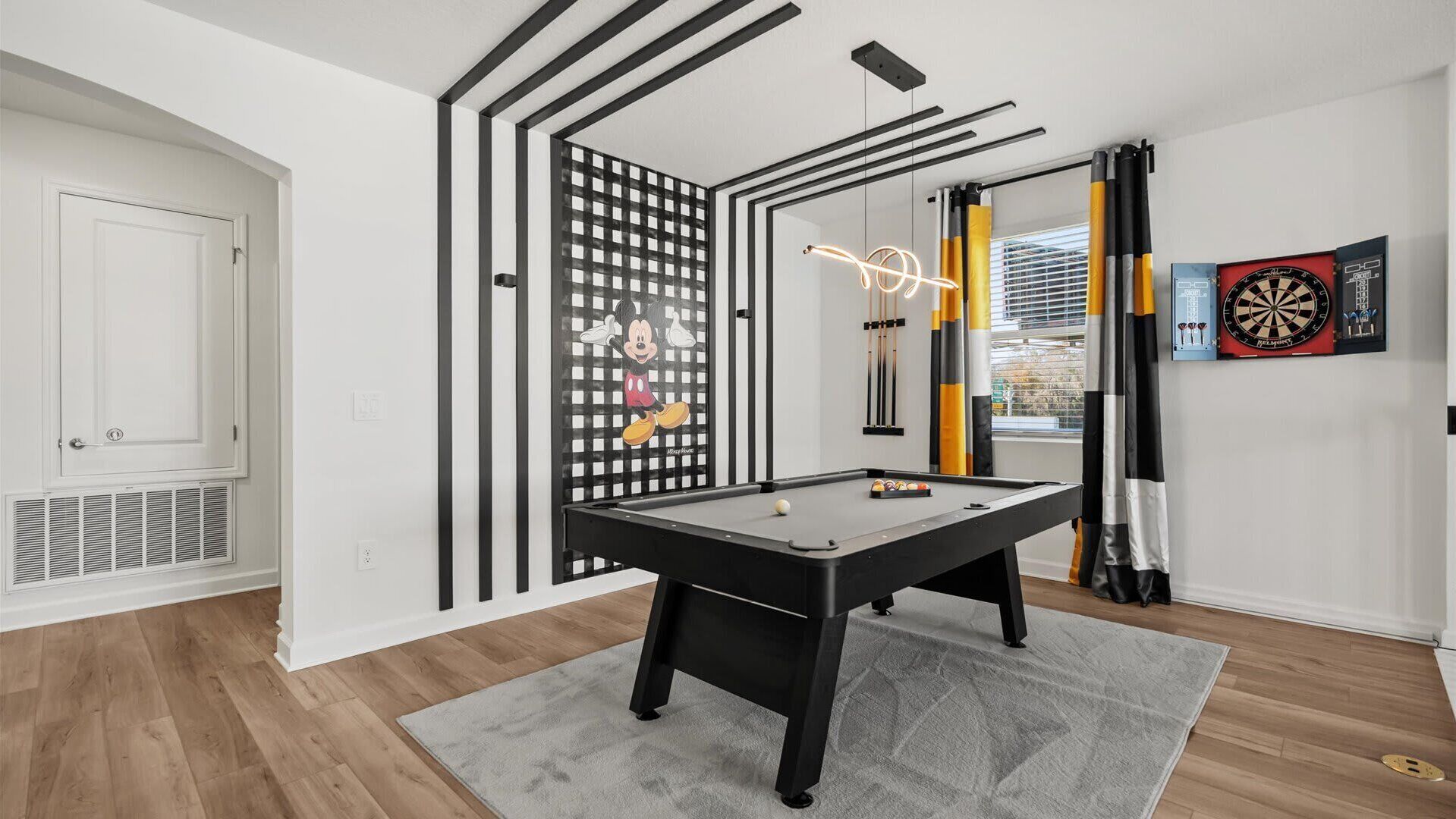 Una habitación con mesa de billar, dardos y un cartel de Mickey Mouse.