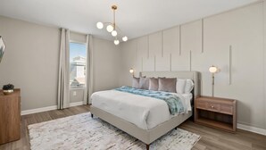 A bedroom with a bed, bedside tables, a nightstand, a wall-mounted light fixture, and a window with curtains. - Family 5BR Villa w Pool Theatre Reunion Village (Kissimmee)