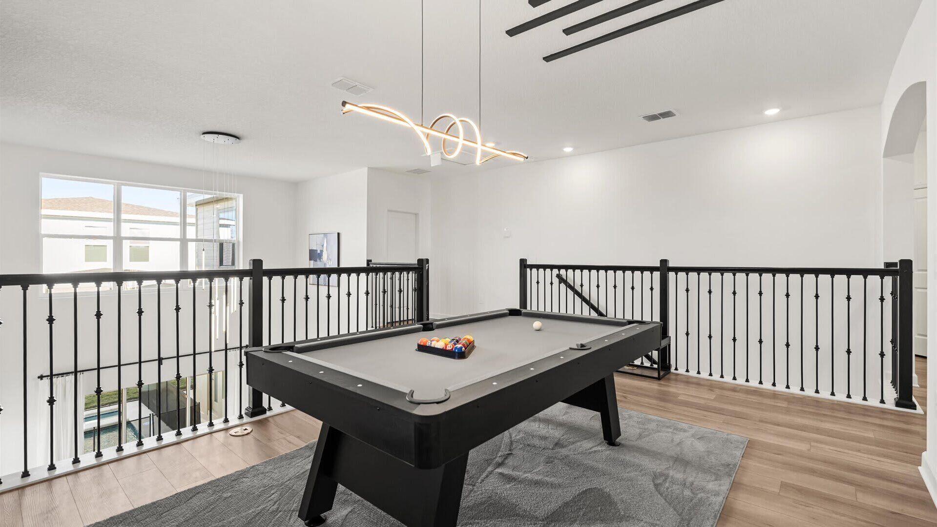A pool table in a modern room with a balcony, white walls, and a view of a building outside.