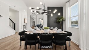 A modern dining area with a rectangular table set for six, black chairs, and a unique ceiling light fixture. - Family 5BR Villa w Pool Theatre Reunion Village (Kissimmee)