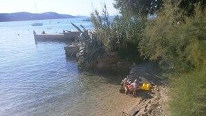 A beach with clear water, a rocky shore, and a few boats in the distance. - Charming Apartment in Stara Novalja (Novalja)