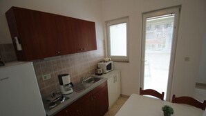 A compact kitchen with a refrigerator, coffee maker, microwave, and a window with blinds. - Charming Apartment in Stara Novalja (Novalja)
