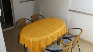 A small dining area with a round table covered by a yellow tablecloth, surrounded by wicker chairs with blue and yellow cushions. - Charming Apartment in Stara Novalja (Novalja)