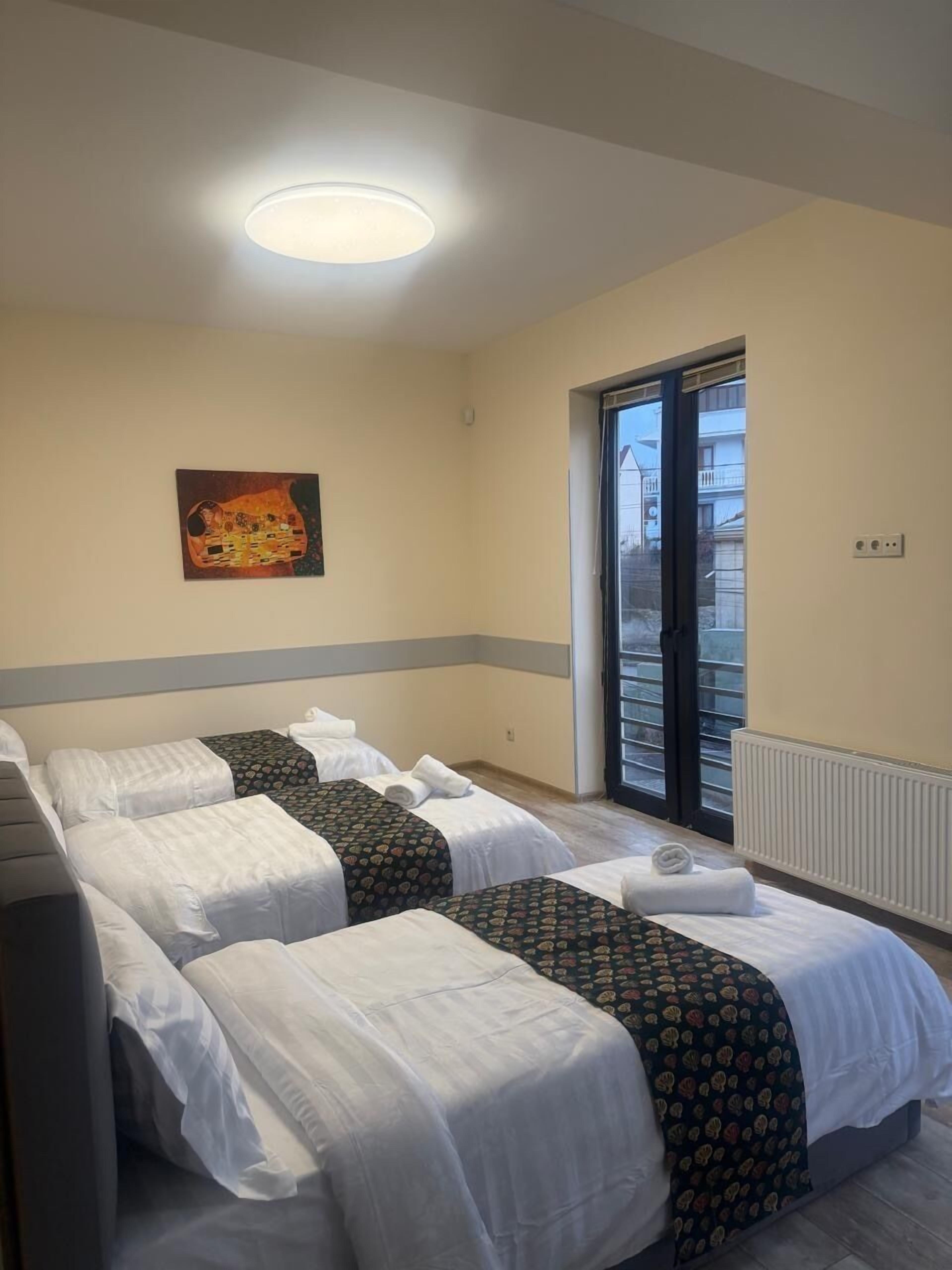 A hotel room with two beds, a painting on the wall, and a window with a view.