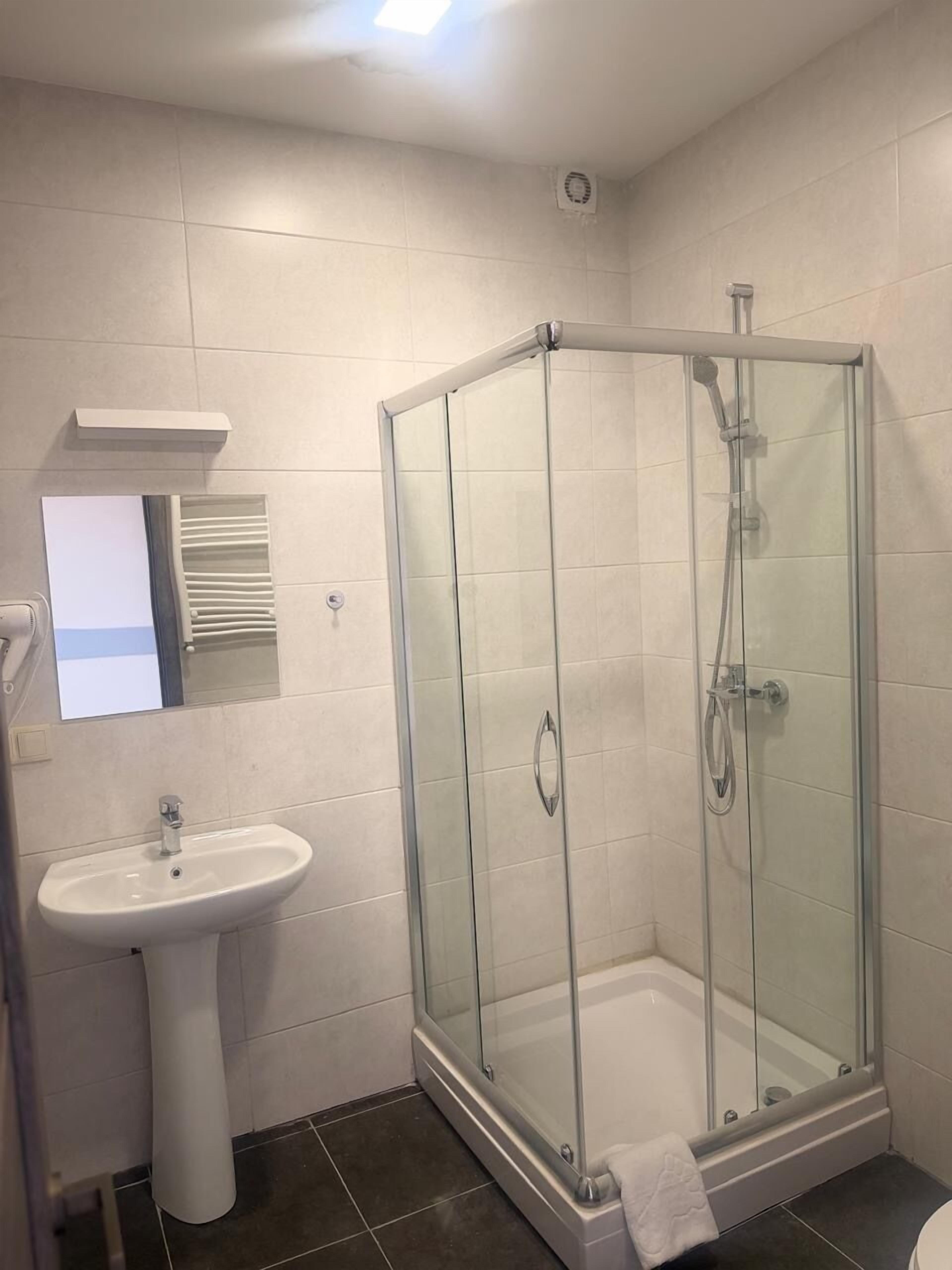 Un baño con ducha de vidrio, lavamanos sobre pedestal y espejo sobre el lavamanos.