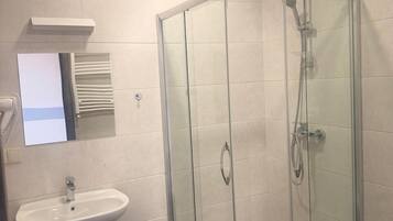 Un baño con ducha de vidrio, lavamanos sobre pedestal y espejo sobre el lavamanos.