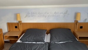 Una cama doble con cabecera, dos mesitas de noche y una pared con una frase decorativa en alemán.