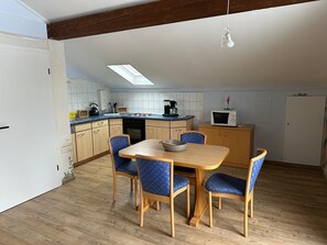 A compact kitchen with a dining area, featuring a skylight, wooden cabinets, a microwave, and a dining table with chairs. - Rapunzel vacation apartment: plenty of space for 4 people & own terrace (Frielendorf)