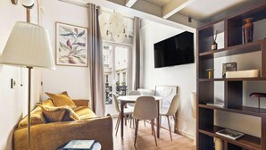 Ein Wohnzimmer mit einer Couch, einem Tisch, Stühlen, einem Fernseher und einem Bücherregal.