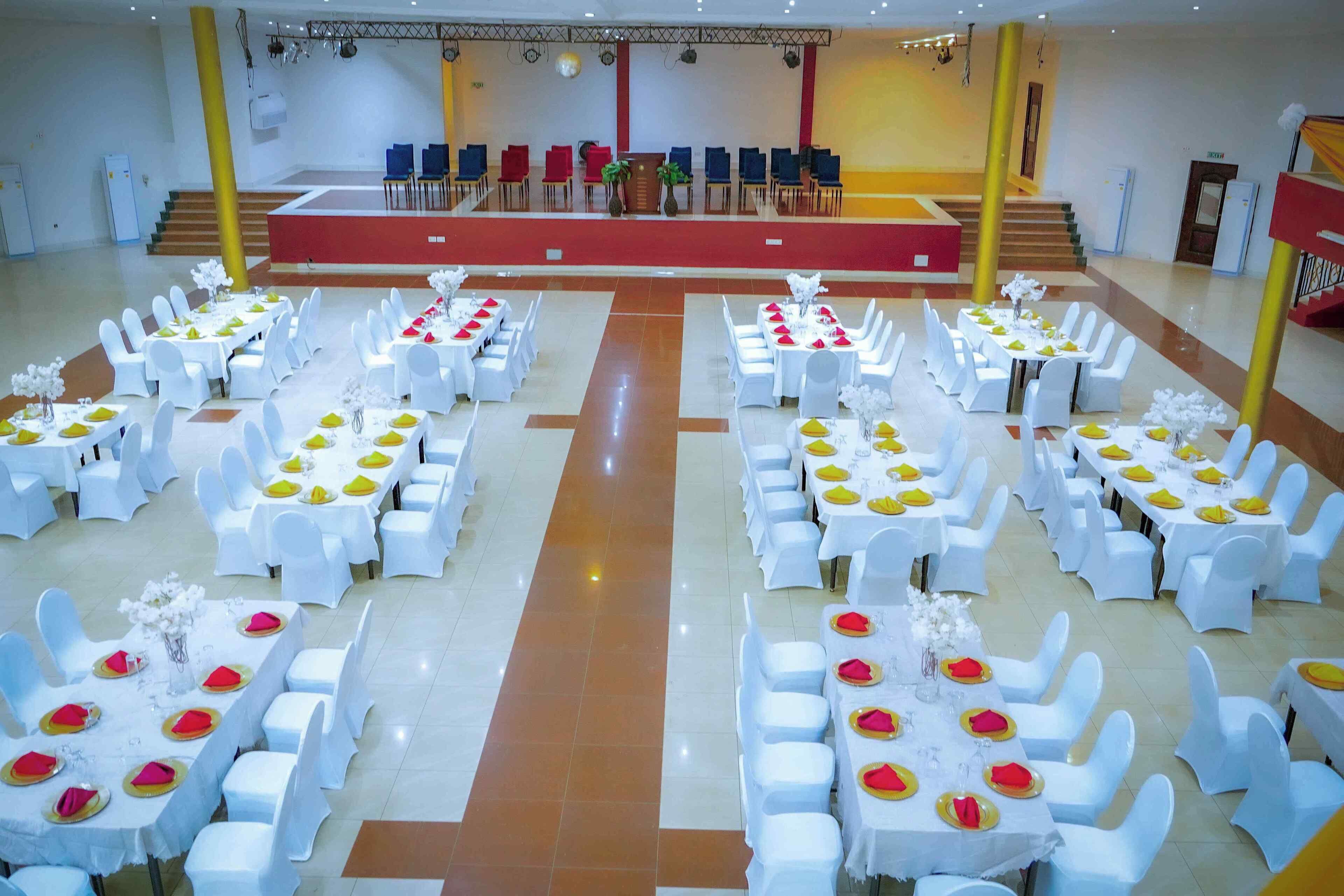 A banquet hall with multiple round tables, each set with white tablecloths, white chairs, and red napkins.