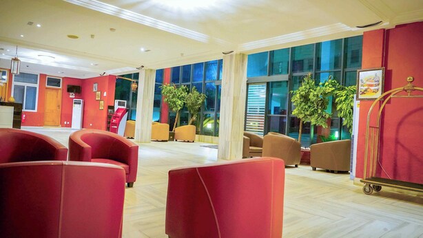 Een hotel lobby met rode zitplaatsen, grote ramen en kamerplanten.