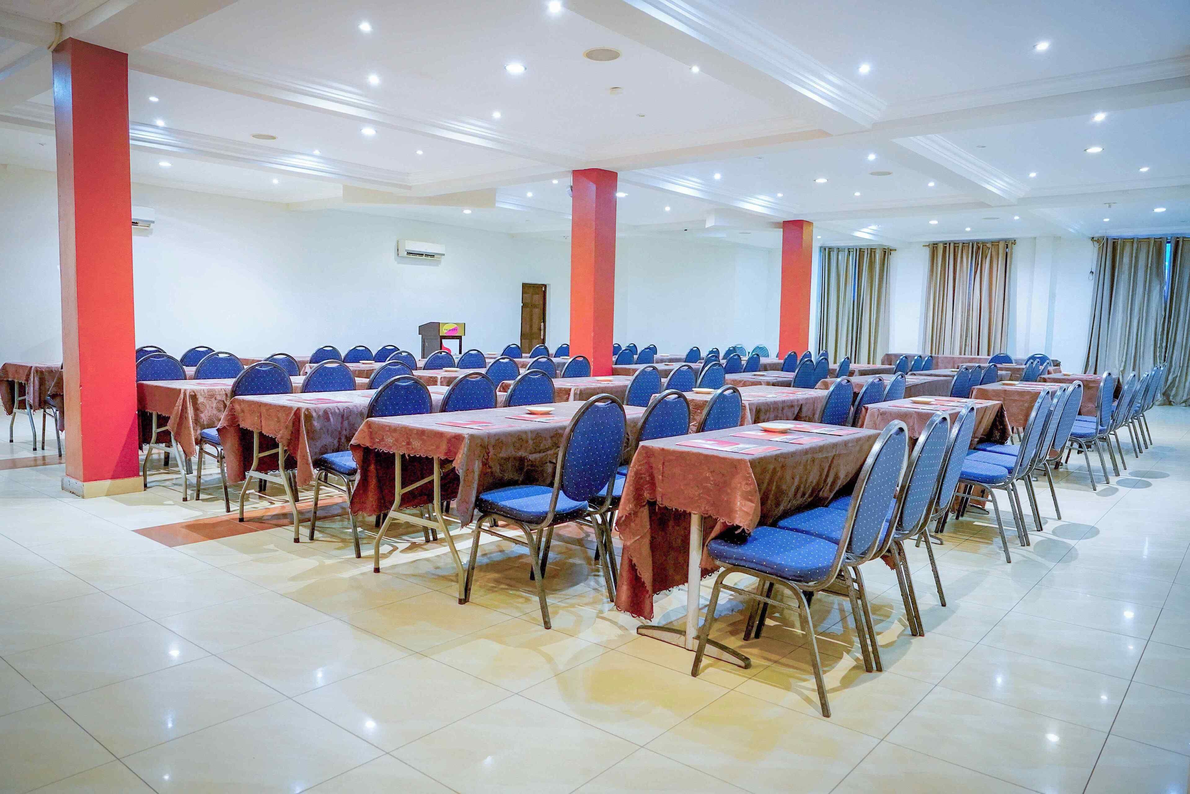 A conference room with rows of tables and chairs, red pillars, and a tiled floor.