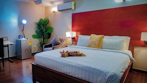 Een hotelkamer met een groot bed, nachtlampjes, een bureau met een lamp, een kleine koelkast en een potplant.
