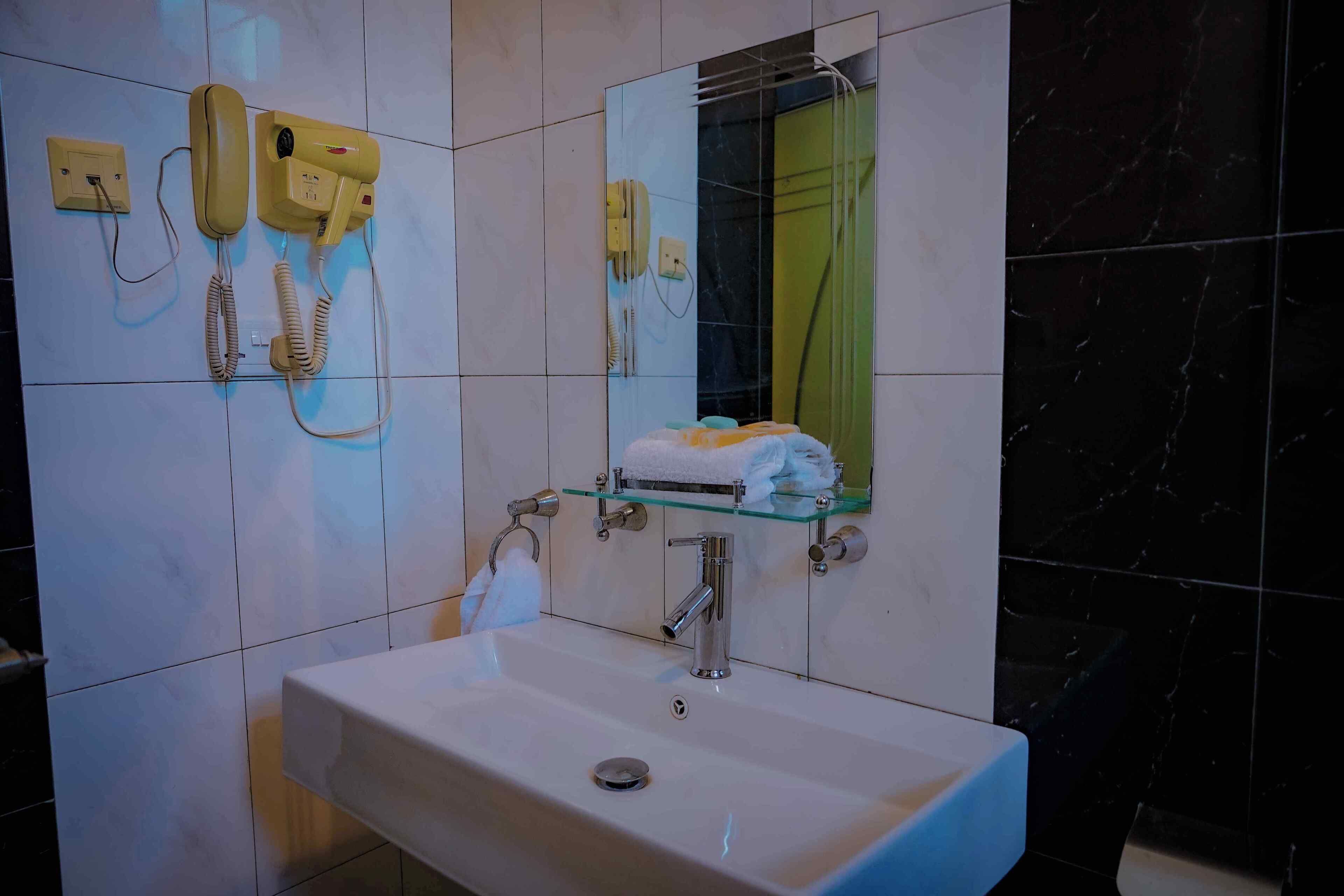 Un baño con un lavamanos blanco, un estante de vidrio con artículos de aseo, un espejo y dos secadores de pelo amarillos montados en la pared.