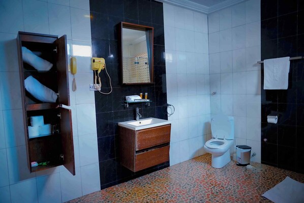 A bathroom with a wooden cabinet, a sink, a toilet, and a mirror. - Tyco City Hotel (Sunyani)