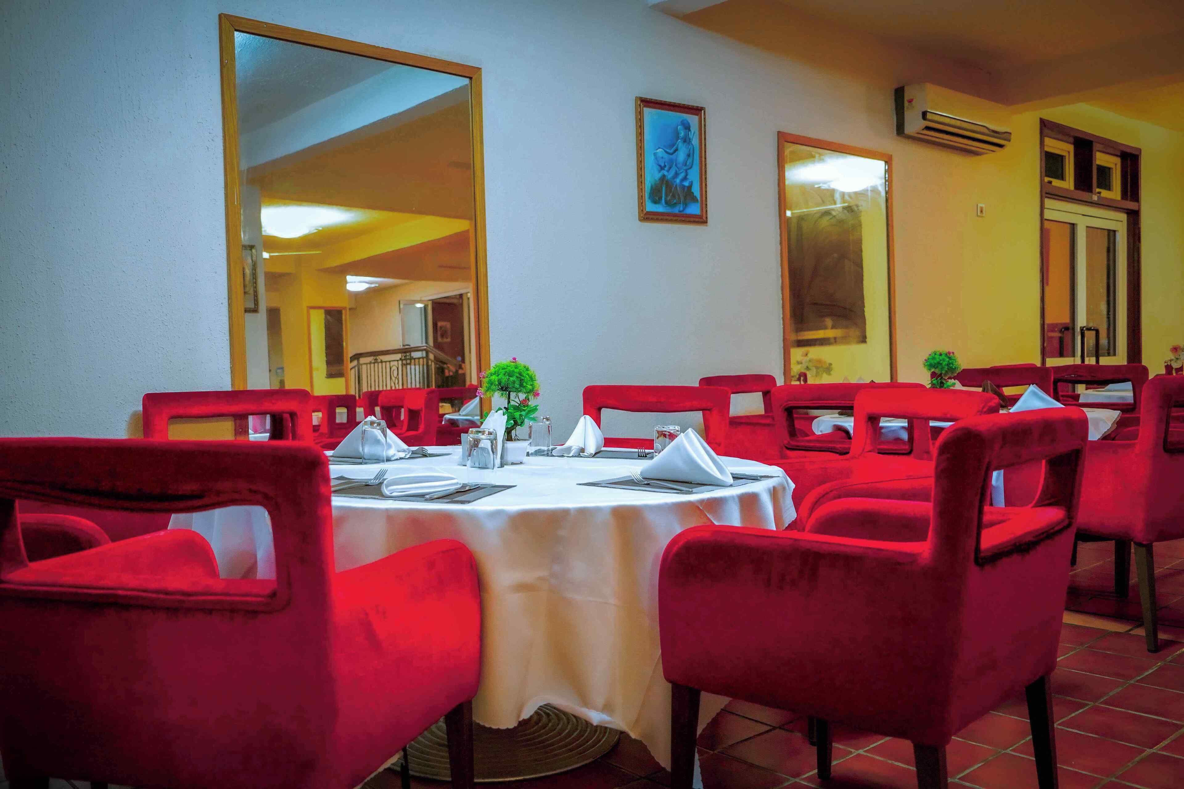 A dining area with red chairs and a round table, a large mirror, and a framed picture on the wall.