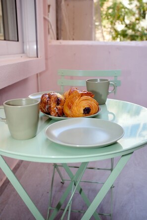 A table with a plate, a cup, and a pastry on a light green chair. - Emily in Athens - Central balcony flat (Athina)