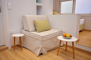A compact living space with a sofa, a small table with fruit, and a window. - Emily in Athens - Central balcony flat (Athina)